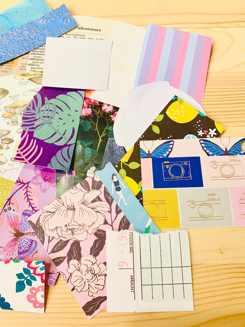 Peut inclure: Un assortiment de papiers d&eacute;coup&eacute;s aux motifs color&eacute;s, dont des fleurs, des feuilles tropicales, des papillons et un carnet de ch&egrave;ques. Les papiers d&eacute;coup&eacute;s sont dispos&eacute;s sur une surface en bois.