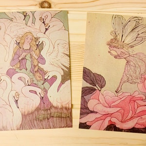 May include: Two vintage-style postcards. One features a woman in a purple dress surrounded by swans. The other shows a fairy with large wings near pink roses. Both have a soft, antique color palette.