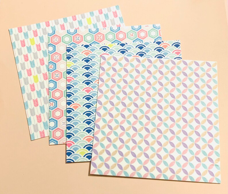 May include: Four sheets of patterned paper with pastel designs. The patterns include arrows, hexagons, waves, and interlocking circles. The colour palette features pink, blue, yellow, and purple on a cream background. The papers are arranged in a layered fan shape.