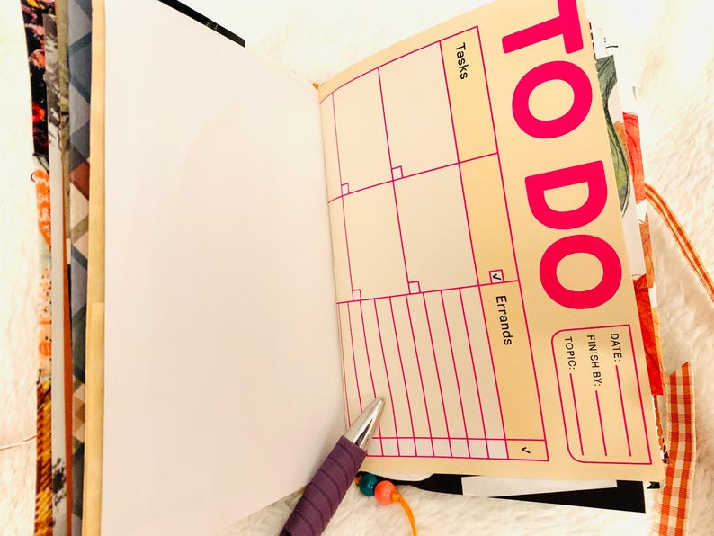 Peut inclure: Un agenda ouvert avec une page couleur cr&egrave;me pr&eacute;sentant un en-t&ecirc;te TO DO rose vif, une grille pour les t&acirc;ches et une section pour les courses. La page inclut des champs pour la date, l'&eacute;ch&eacute;ance et le sujet. Un stylo violet avec une breloque perl&eacute;e repose sur la page.