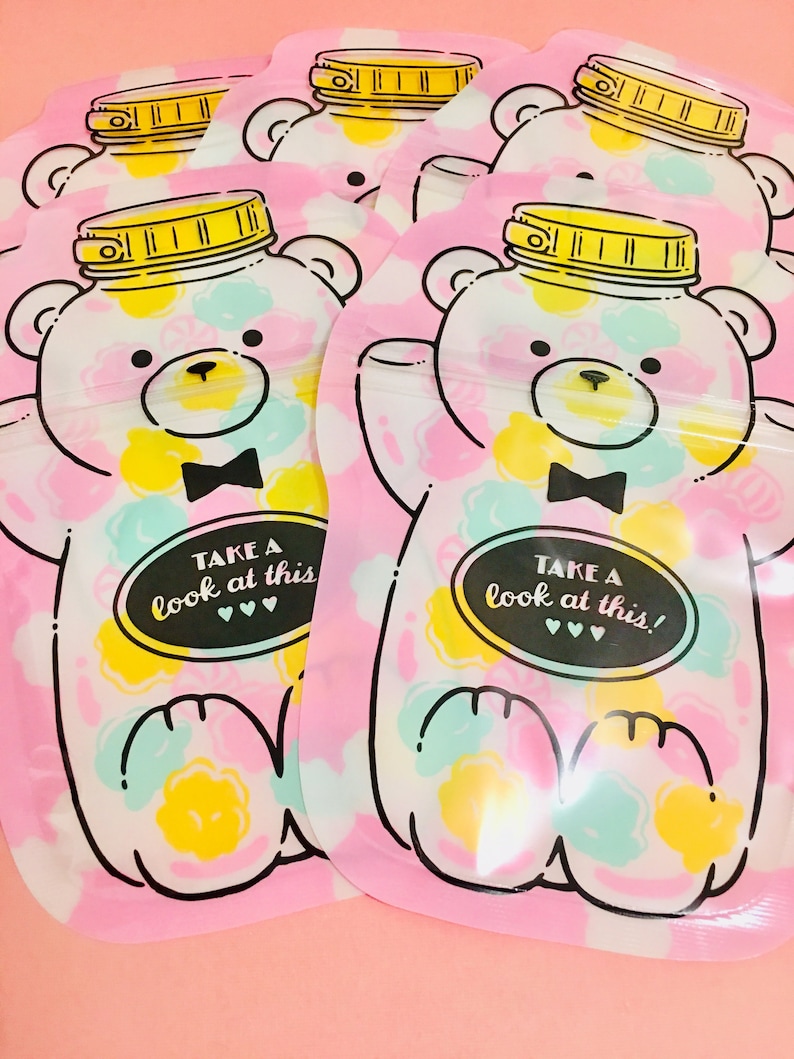 May include: Four pink reusable snack bags with a bear design. Each bag has a white bear with a black bow tie and a jar of colorful candies on its head. The bags have the text "Take a look at this!" printed on them.