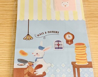 May include: A clear plastic bag containing a decorative paper bag and a small pink card. The paper bag features a cartoon scene with a rabbit chef, a squirrel, and pancakes. The card says "For You" with a fork and knife illustration.