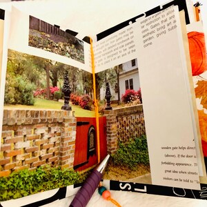 Peut inclure: Un album ouvert pr&eacute;sentant une photographie imprim&eacute;e d'un portail rouge ins&eacute;r&eacute; dans un mur de briques avec des fleurons noirs. La page contient du texte noir sur les portails et le jardin. Un stylo violet avec une perle orange et bleue repose dessus.