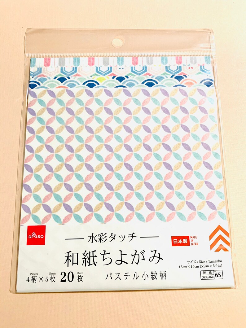 May include: A pack of DAISO origami paper featuring pastel geometric patterns. The pack contains 20 sheets, each 15cm x 15cm, with four different designs. The text on the package is in Japanese.