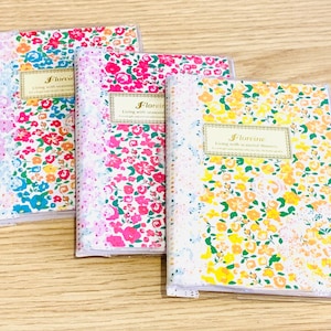 Könnte beinhalten: Vier kleine Notizbücher mit floralem Muster und goldener Aufschrift "Florene Leben mit saisonalen Blumen".