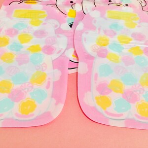May include: Two pink plastic face masks with a bear design. The bears are filled with colorful candy-like shapes. The masks are packaged individually.