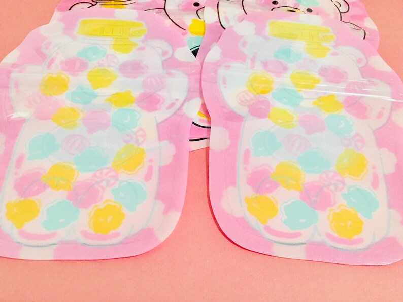 May include: Two pink plastic face masks with a bear design. The bears are filled with colorful candy-like shapes. The masks are packaged individually.