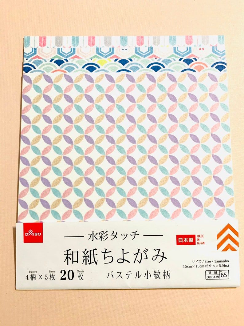 May include: A pack of Japanese origami paper with a pastel geometric pattern. The paper features a repeating design of overlapping circles in shades of pink, purple, yellow, and blue. The package includes Japanese text and measures 15cm x 15cm.
