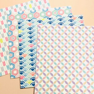 May include: A selection of patterned paper sheets in pastel shades. Designs include arrows, hexagons, waves, and interlocking circles. The papers are arranged on a light peach background, showcasing the variety of patterns.