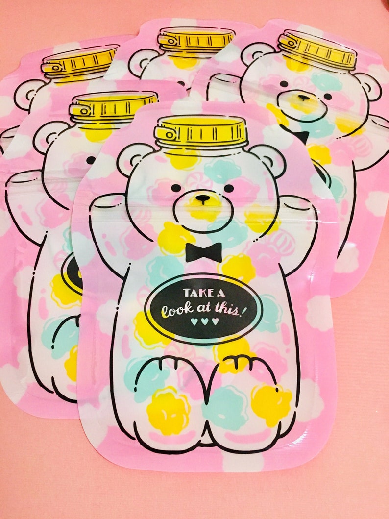 May include: A set of five pink reusable snack bags with a white bear design. The bear is wearing a black bow tie and has a jar lid on its head. The bags have a white background with colorful polka dots and the text "TAKE A look at this!" in a black oval.