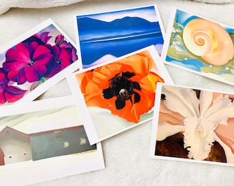 Op de afbeelding: Een verzameling kunstafdrukken met bloemen- en landschapsschilderijen. De afdrukken tonen levendige kleuren en gedetailleerde penseelstreken, met onderwerpen als bloemen, een zeeschelp en een schuur. De afdrukken worden op een wit oppervlak gepresenteerd.