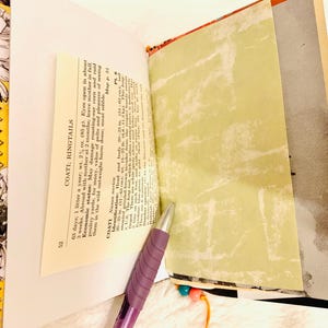 Peut inclure: Un journal fait main avec une reliure en tissu aux motifs orange et noirs. Les pages ouvertes pr&eacute;sentent un texte imprim&eacute; intitul&eacute; COATI; RINGTAILS avec des d&eacute;tails incluant un poids de 85 g et une longueur de corps de 51-63 cm. Un stylo violet est pos&eacute;.