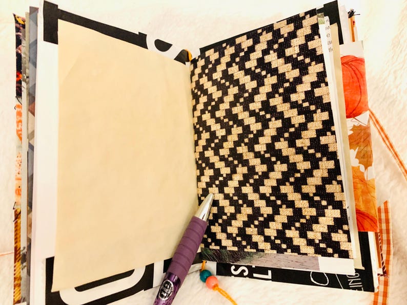 Peut inclure: Un journal ouvert avec une page vierge couleur cr&egrave;me &agrave; gauche et une page avec un motif g&eacute;om&eacute;trique noir et beige style tiss&eacute; &agrave; droite. Un stylo violet avec une prise textur&eacute;e repose en diagonale sur le bas des pages ouvertes.