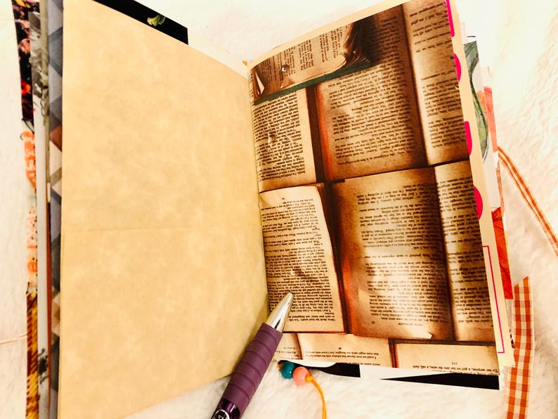Peut inclure: Un journal ouvert pr&eacute;sentant une page vierge beige clair et une page avec un collage de texte de livre ancien. Un stylo violet &agrave; pointe argent&eacute;e repose au bas du journal. Les pages sont reli&eacute;es par des perles color&eacute;es sur un fil &agrave; la base.