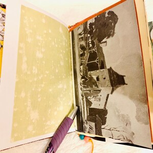 Peut inclure: Un journal ouvert avec une page vert clair &agrave; gauche et une illustration en noir et blanc d'un b&acirc;timent &agrave; droite. Un stylo violet repose sur le bas des pages. La reliure et les bords pr&eacute;sentent un tissu &agrave; motifs orange et noir.