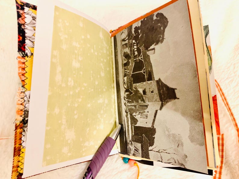 Peut inclure: Un journal ouvert avec une page vert clair &agrave; gauche et une illustration en noir et blanc d'un b&acirc;timent &agrave; droite. Un stylo violet repose sur le bas des pages. La reliure et les bords pr&eacute;sentent un tissu &agrave; motifs orange et noir.
