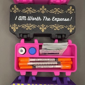 May include: Three rectangular plastic storage cases with hinged lids. The top case is pink with a leopard print and the text SHOTS HAPPEN. The middle case is black with gold fleur-de-lis and the text I Am Worth The Expense!, containing syringes, vials, and alcohol pads. The bottom case is purple with a yellow zebra print and the text Lookin' Wild Eating Mild.