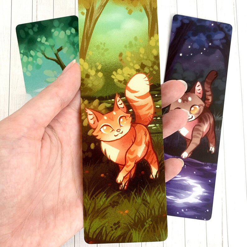 May include: Three illustrated bookmarks featuring a cat in a forest, a cat in a starry night sky, and a green forest scene. The bookmarks are printed on cardstock and are approximately 6 inches tall.