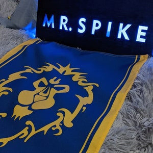 Op de afbeelding: Een blauwe en gele vlag met een gouden leeuwenembleem en de tekst "MR. SPIKE" op een zwart bord met blauwe LED-verlichting.