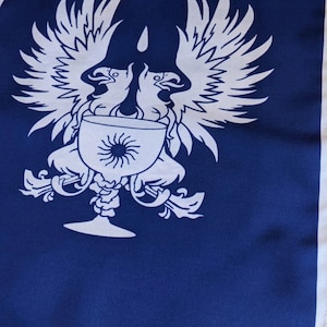 May include: A blue flag with a white design of two birds with outstretched wings holding a chalice with a sun inside. The chalice has a decorative stem and base.