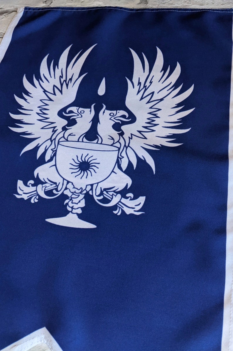 May include: A blue flag with a white design of two birds with outstretched wings holding a chalice with a sun inside. The chalice has a decorative stem and base.