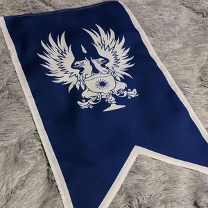 May include: A blue fabric flag with a white design of two birds with outstretched wings, a sun, and a goblet. The flag is a pennant shape with a white border.