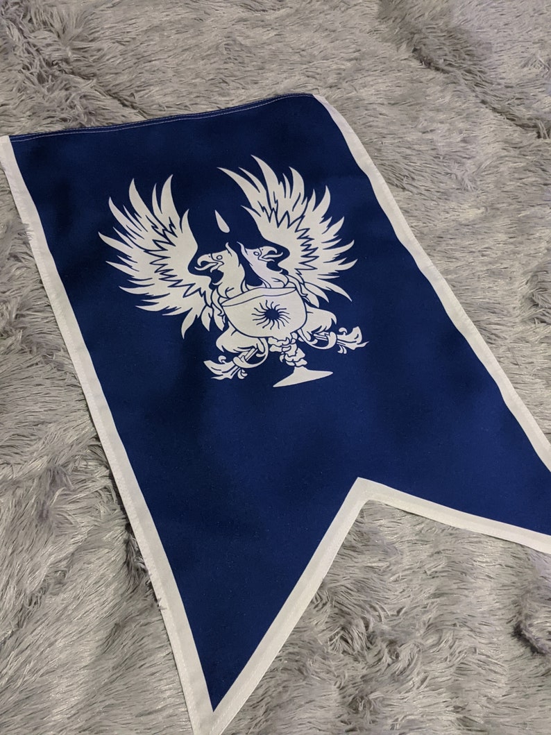 May include: A blue fabric flag with a white design of two birds with outstretched wings, a sun, and a goblet. The flag is a pennant shape with a white border.