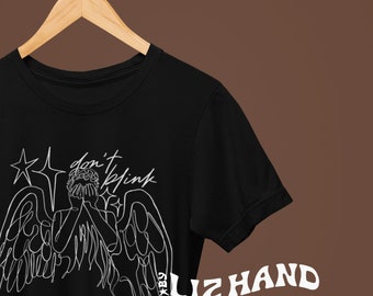 May include: Black t-shirt with a white line drawing of a weeping angel with the text "don't blink" and the signature "Liz Hand" in white.