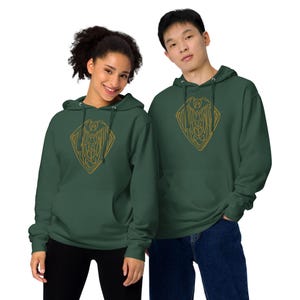 May include: Two people wearing matching forest green hoodies. Each hoodie features a gold-colored geometric design on the front. The hoodies have a front pocket and a hood with drawstrings. The person on the left is wearing black pants, and the person on the right is wearing blue jeans.