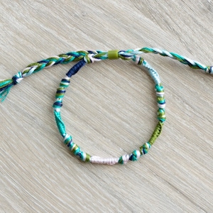 May include: A braided friendship bracelet with green, blue, white, and pink threads. The bracelet is tied with a green knot.
