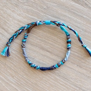 May include: A braided friendship bracelet with blue, brown, and gray threads. The bracelet has a small blue bead at the top.