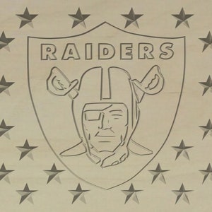 May include: A black and white image of the Las Vegas Raiders logo. The logo is a shield with the word "RAIDERS" at the top and a stylised image of a pirate's head in the centre.