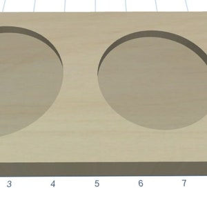 May include: A wooden tray with two circular cutouts, probably for holding cups or glasses. The tray is made of light-coloured wood and has a smooth surface.