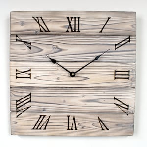 May include: A rustic wooden clock with Roman numeral markings and black hands. The clock face is made of reclaimed wood planks.