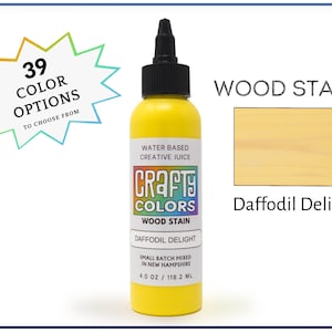 May include: A 4 ounce bottle of Crafty Colors wood stain in the color Daffodil Delight. The bottle is yellow and has a label with the company logo and product information. The stain is water-based and small batch mixed in New Hampshire.