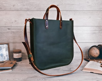 May include: A dark green vertical tote bag featuring two brown leather handles secured with metal rivets and a long, adjustable brown leather shoulder strap. The bag has a structured, rectangular body with rounded bottom corners and a smooth finish.