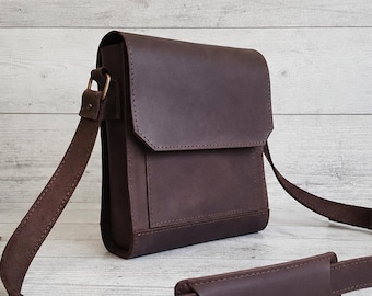 May include: A dark brown leather messenger bag featuring a rectangular flap closure, a front pocket, and an adjustable shoulder strap with a sliding padded section. The bag is constructed with visible stitching along the edges and sides.