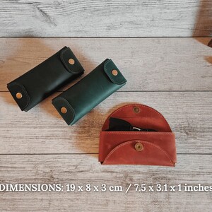 May include: Three leather cases in shades of green and red-orange are displayed on a wooden surface. The cases are closed with a snap closure. The dimensions are 7.5 x 3.1 x 1 inches.