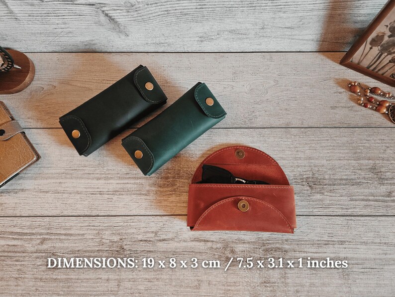 May include: Three leather cases in shades of green and red-orange are displayed on a wooden surface. The cases are closed with a snap closure. The dimensions are 7.5 x 3.1 x 1 inches.