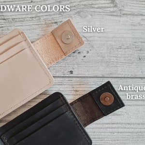 Pu&ograve; includere: Due portafogli in pelle, uno beige e uno nero, con chiusure magnetiche. Il portafoglio beige ha un bottone a pressione argentato, mentre quello nero ha un bottone a pressione in ottone anticato. Il testo "HARDWARE COLORS" &egrave; in alto.