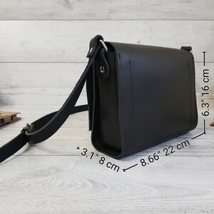 May include: A black leather crossbody bag with a rectangular shape, a flap closure, and an adjustable shoulder strap. The bag measures 8.66 inches in length, 6.3 inches in height, and 3.1 inches in depth, as indicated by the visible measurement text.