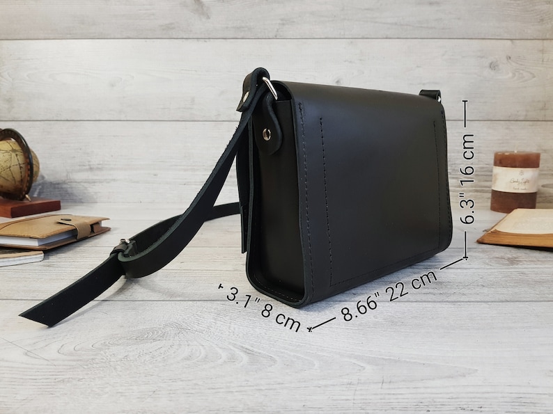 May include: A black leather crossbody bag with a rectangular shape, a flap closure, and an adjustable shoulder strap. The bag measures 8.66 inches in length, 6.3 inches in height, and 3.1 inches in depth, as indicated by the visible measurement text.