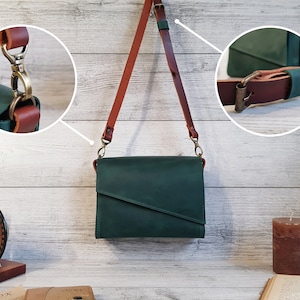 May include: A dark green leather crossbody bag with a diagonal front flap and a long, adjustable brown leather shoulder strap. The bag features antique brass-toned metal hardware, including a swivel lobster clasp and a buckle for strap adjustment.