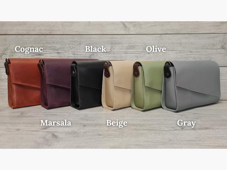 May include: Six rectangular crossbody bags with flap closures, arranged in a row. The colors from left to right are labeled as Cognac, Marsala, Black, Beige, Olive, and Gray. Each bag features a dark brown side tab and a smooth, solid finish.