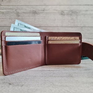 Pu&ograve; includere: Portafoglio in pelle marrone aperto con pi&ugrave; fessure per carte e uno scomparto per contanti. Il portafoglio &egrave; pieno di carte e diverse banconote da cento dollari. Il portafoglio &egrave; aperto, mostrando il suo contenuto.
