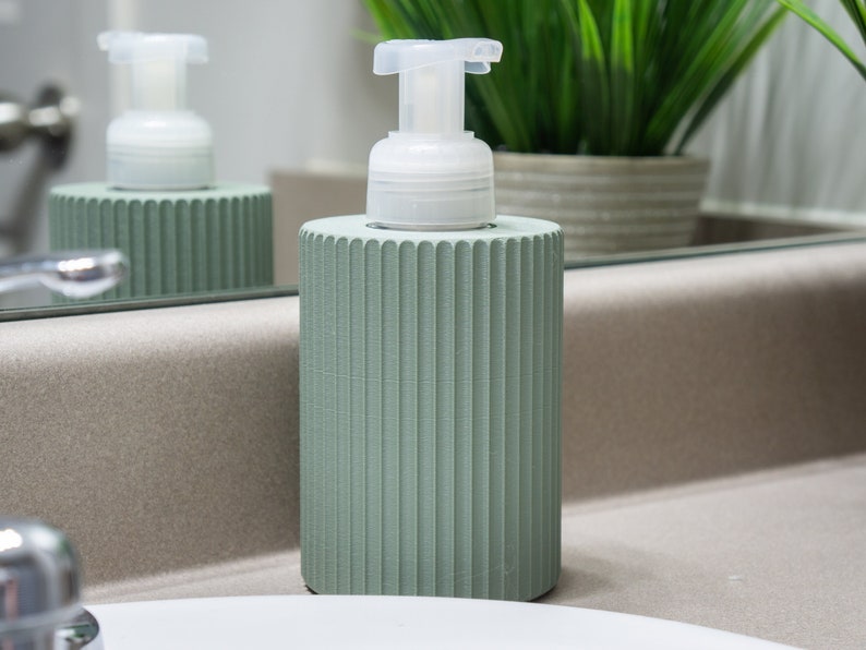May include: A green soap dispenser with a white pump. The dispenser has a ribbed design and is sitting on a counter.