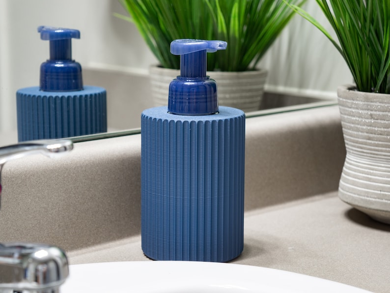 May include: A blue soap dispenser with a ribbed design and a pump top. The dispenser is sitting on a bathroom counter.