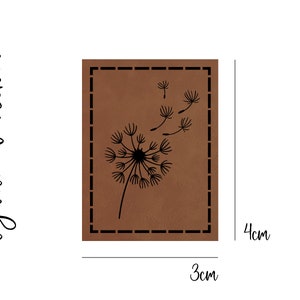 Könnte beinhalten: Ein braunes Lederstück mit einer schwarzen Silhouette eines Löwenzahns mit Samen, die im Wind fliegen. Das Stück misst 3 cm x 4 cm.