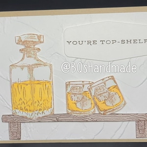 May include: A greeting card with a hand-drawn illustration of a decanter and two glasses of liquor on a shelf. The card has the text "You're Top-Shelf" and the watermark "@BQShandmade".