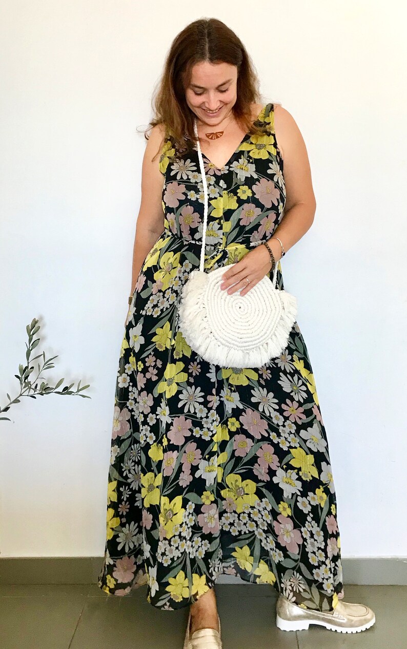 May include: A woman wearing a black maxi dress with a floral print and a white crocheted bag. She is wearing gold sandals.